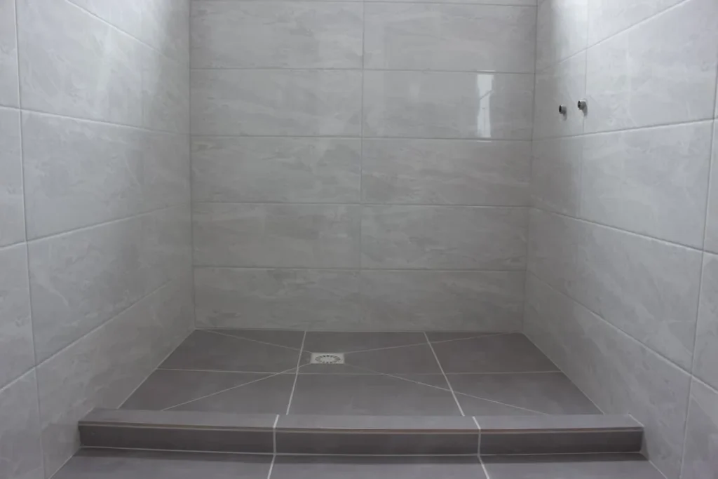 Modern shower room after renovation Sideboard drain in the floor and addition for faucets in the wall Gray tiles on the floor and walls