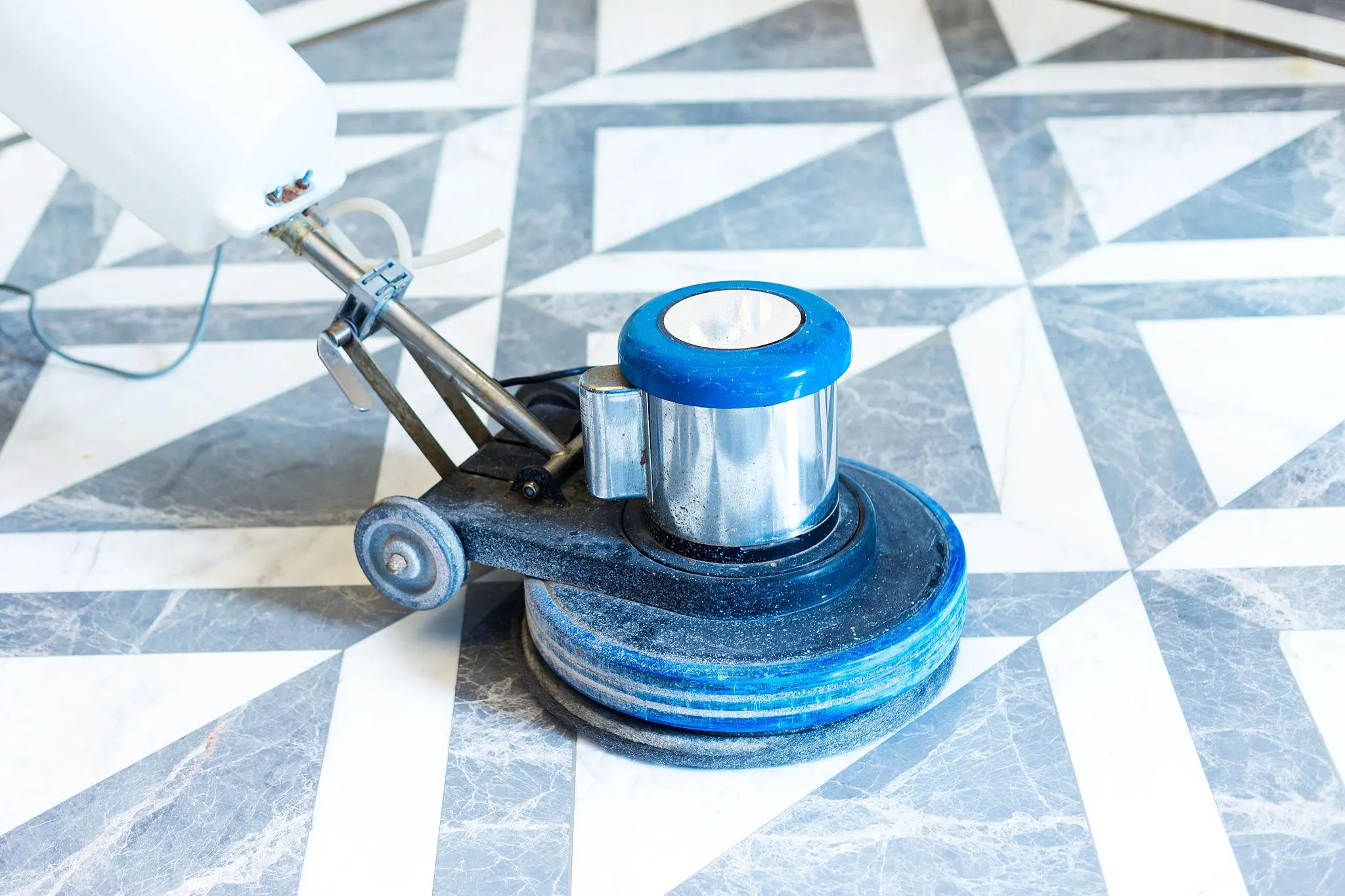 Floor polishing machine with blue top sits on marble-patterned geometric tile floor used for polishing floors.