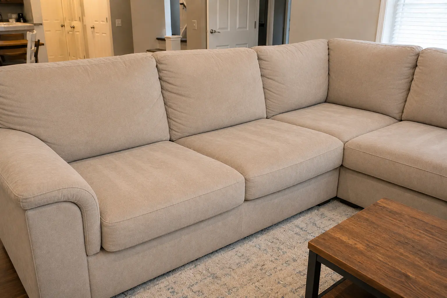 Beige sectional sofa in a living room with a wooden coffee table on a light rug.