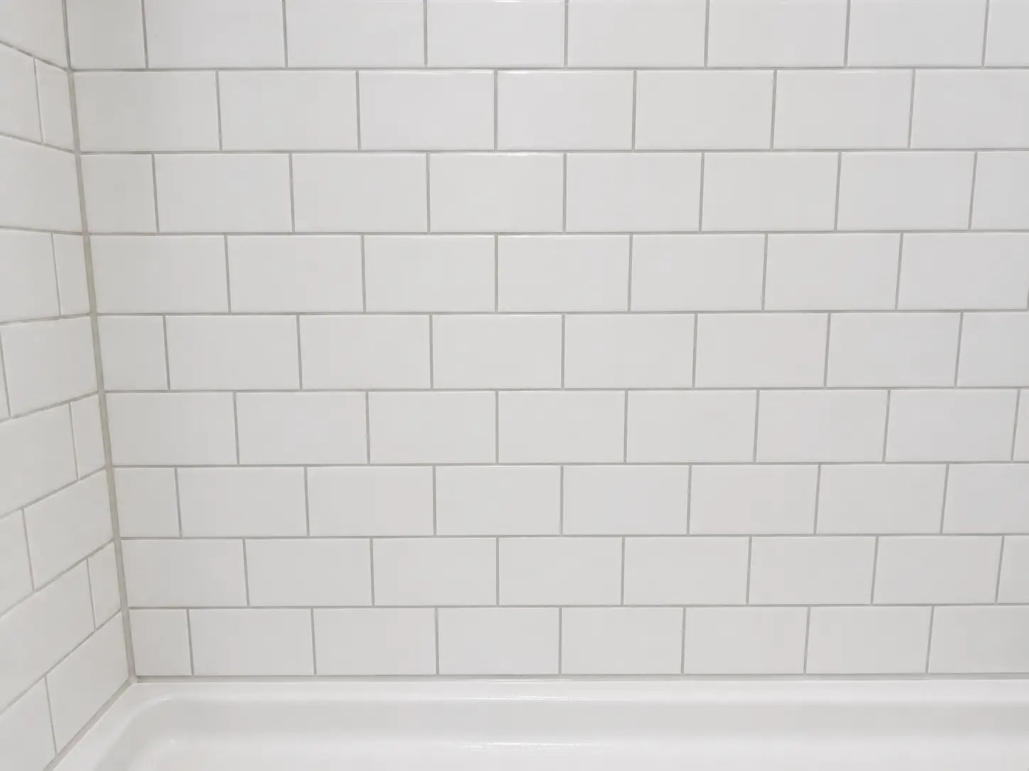 White subway tile bathroom wall with grout lines and the bathtub edge at the bottom.