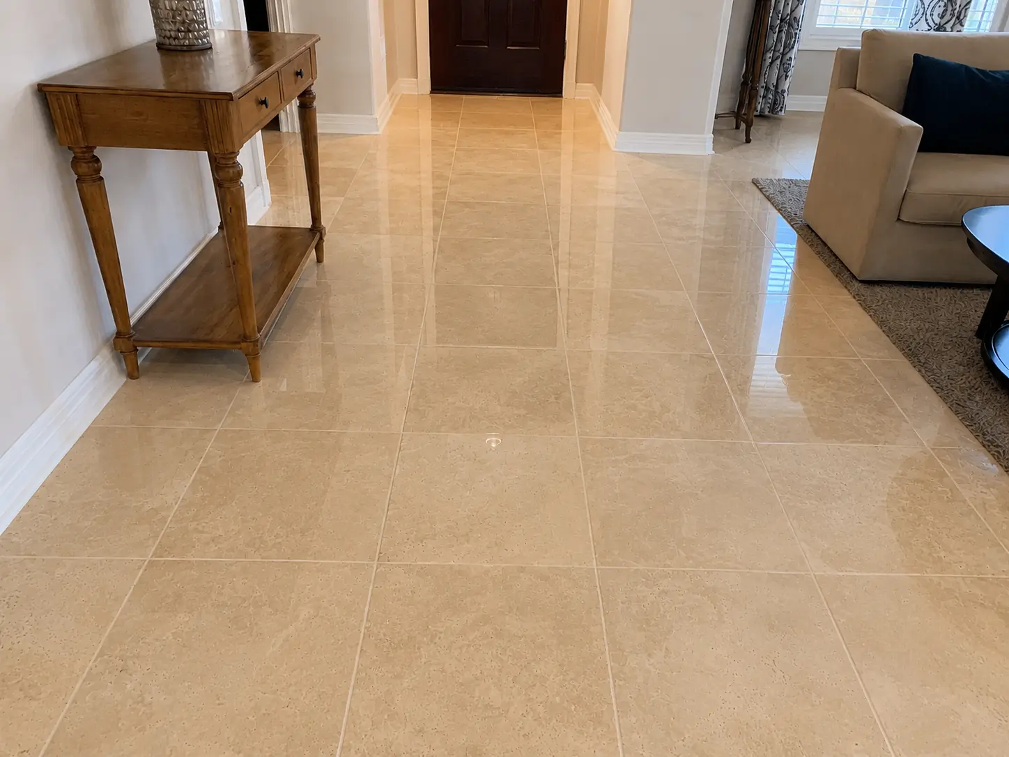 Bright beige tiled foyer with a wooden console table on the left and a dark front door at the end.