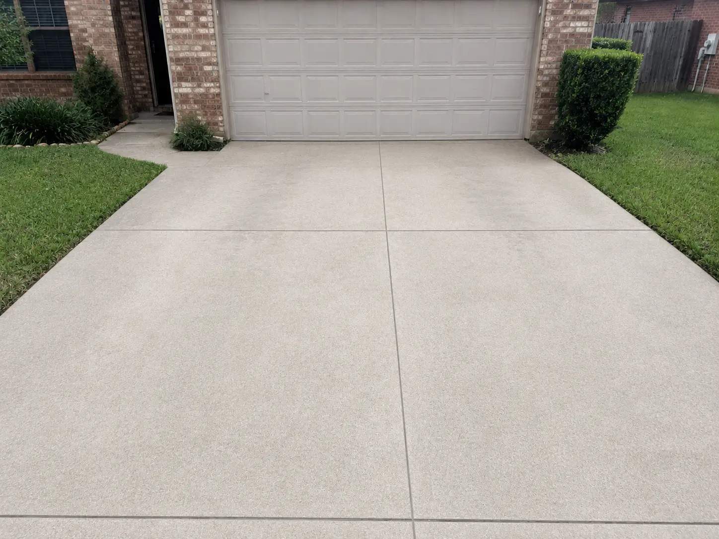 Concrete driveway leading to a closed beige garage door, flanked by brick house and neatly trimmed green lawns and shrubs at the sides.