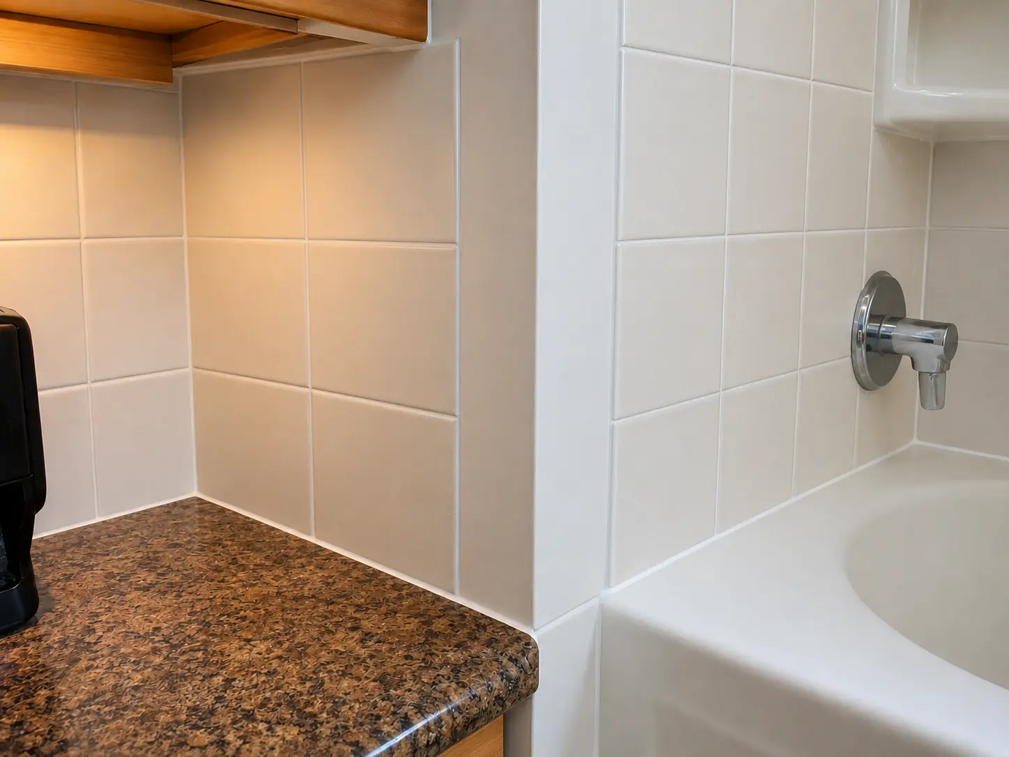Corner of a bathroom with white tile walls, a granite countertop, and a chrome tub faucet mounted on the tub edge.