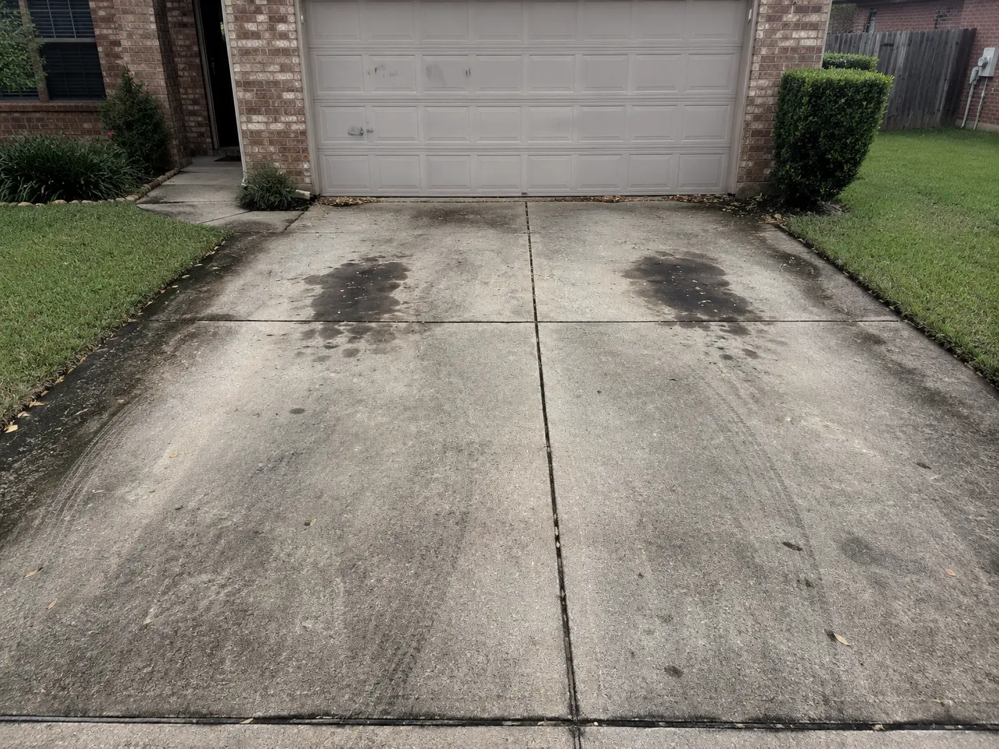 Concrete driveway with two dark wet patches leading to a gray, panelled garage door.