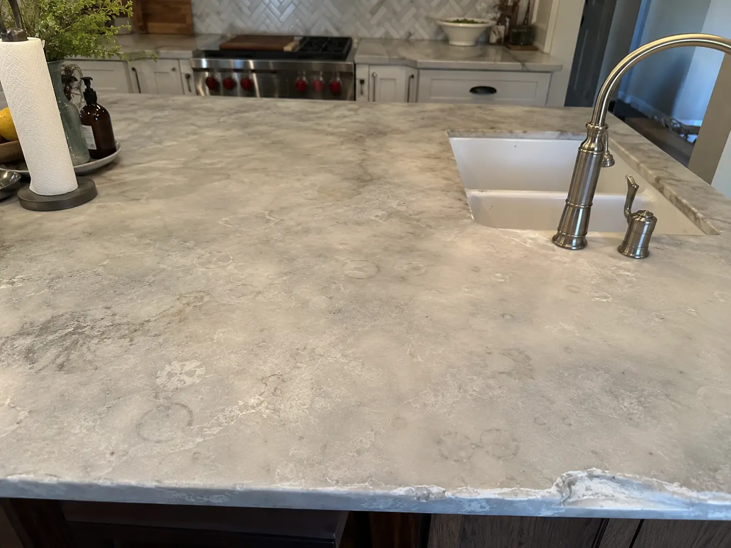 Close-up of a gray marble kitchen island with a built-in sink and curved stainless steel faucet on the right.