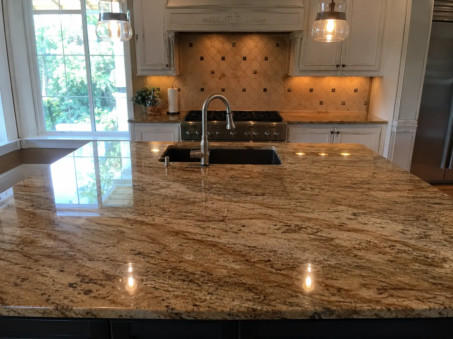 Granite kitchen island with undermount sink and sleek chrome faucet, pendant lights overhead.