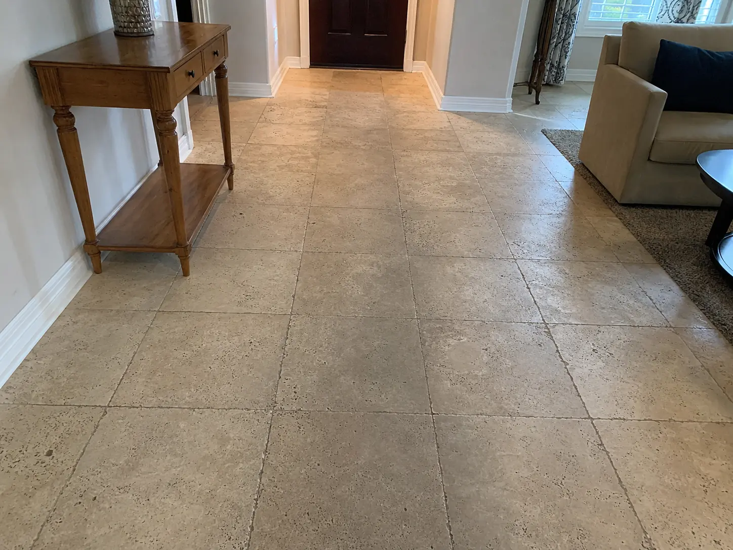 Entry hall with beige tile floor, a wooden console table on the left, and a dark front door straight ahead.