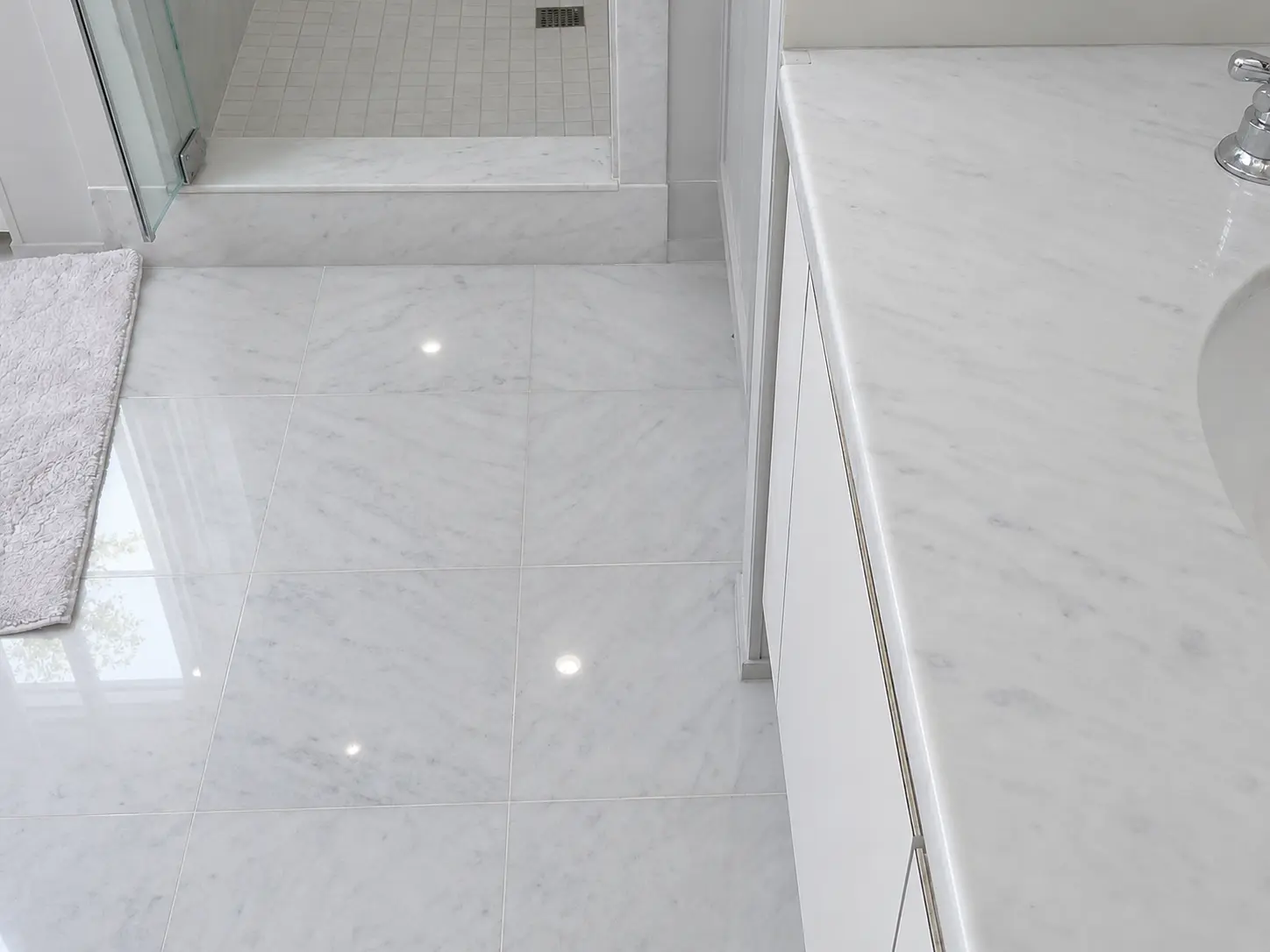 White marble bathroom with a glass shower door, white cabinetry, and a marble countertop along the right wall.
