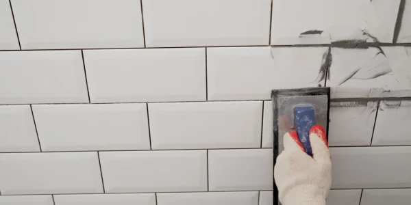 Workers hands using a rubber spatula and grouting with paste between white ceramic tiles Close-up of grout Grouting seams on a tile backsplash